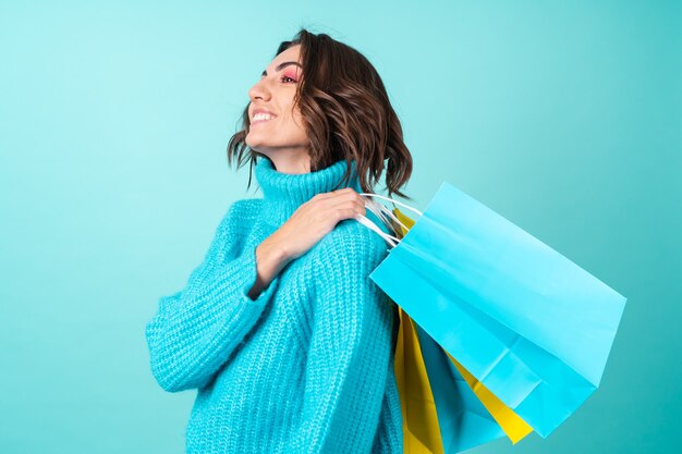 Accogliente ritratto di una giovane donna con un maglione blu lavorato a maglia e un trucco rosa brillante su borse della spesa turchesi