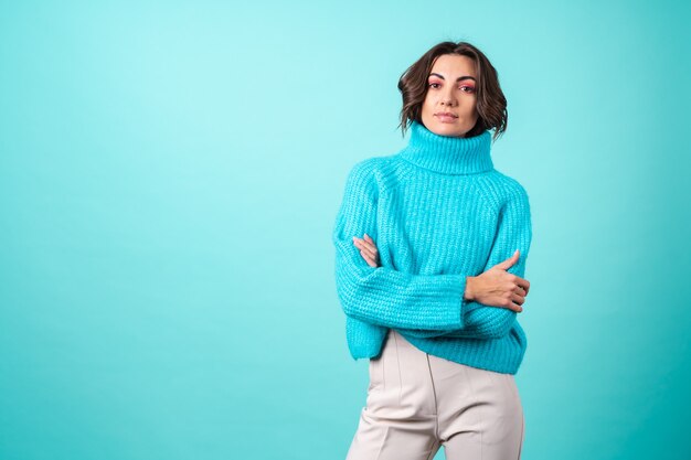 Accogliente ritratto di una giovane donna con un maglione blu lavorato a maglia e un trucco rosa brillante su turchese