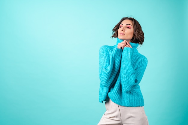 Accogliente ritratto di una giovane donna con un maglione blu lavorato a maglia e un trucco rosa brillante su turchese