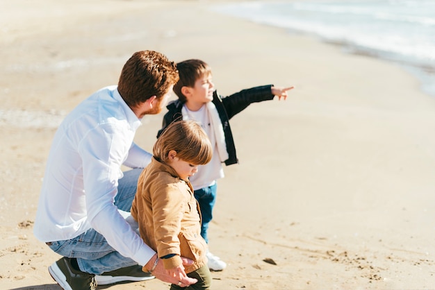 Accovacciare il padre con i figli sulla spiaggia