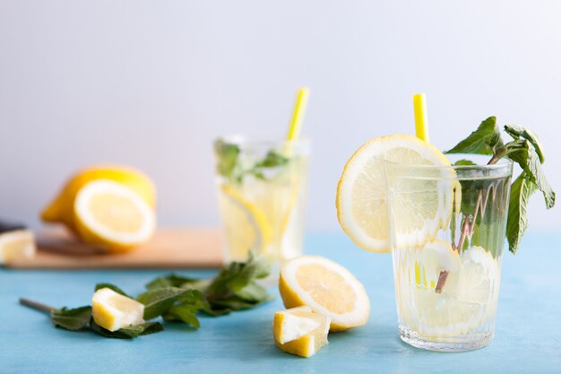 Acqua detox fresca fatta in casa con limoni su sfondo grigio e seduta su una scrivania vintage blu