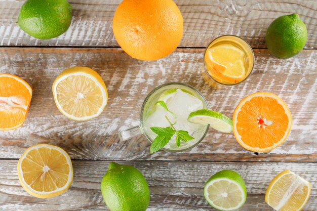 Acqua disintossicante con lime, limoni, arance, menta in tazza e vetro su superficie di legno, piatto disteso.
