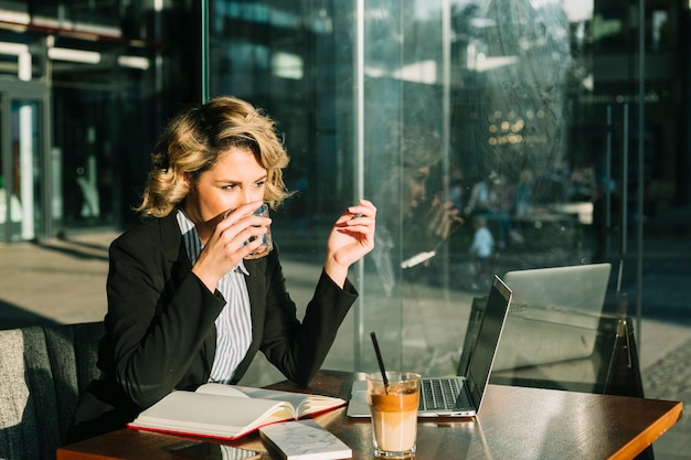 Acqua potabile della donna di affari con il frappè del cioccolato e del computer portatile sullo scrittorio