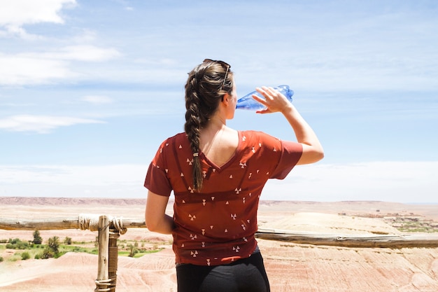 Acqua potabile della donna nel paesaggio del deserto da dietro