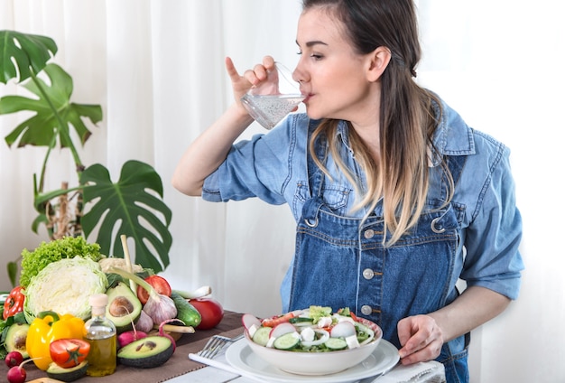 Acqua potabile della giovane donna al tavolo con le verdure