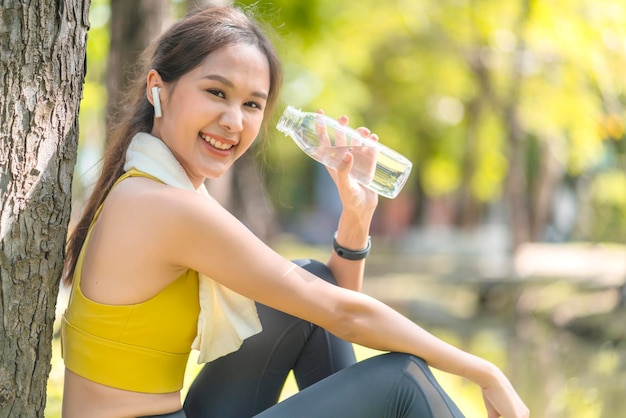 Acqua potabile della giovane donna dalla bottiglia dell'acqua potabile femminile asiatica dopo gli esercizi o lo sport Bella donna dell'atleta di forma fisica che indossa il cappello dell'acqua potabile dopo l'allenamento che si esercita sulla sera del tramonto