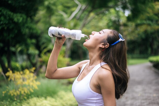 Acqua potabile della giovane donna in buona salute dalle bottiglie di plastica dopo avere pareggiato.