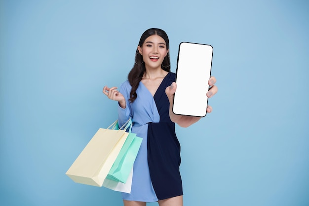 Acquirente asiatico donna che si gode lo shopping sta portando borse per la spesa e mostra lo schermo vuoto del telefono
