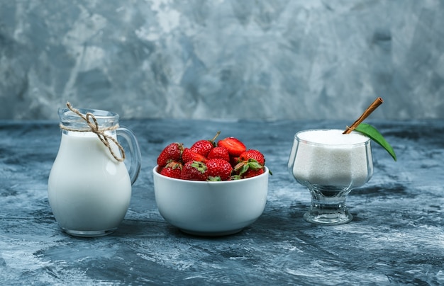 Adagiare una ciotola di fragole su un asciugamano a quadretti rosso e una brocca di latte e una ciotola di vetro di yogurt su una superficie di marmo blu scuro. spazio libero orizzontale per il testo
