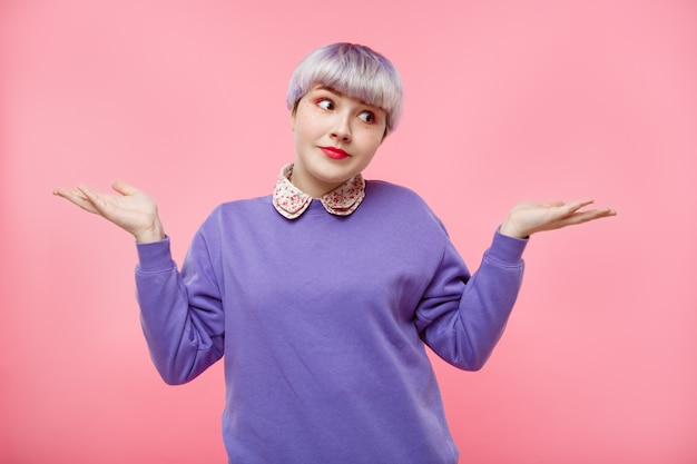 Adatti il ritratto del primo piano di bella ragazza da bambola sorpresa con i capelli di breve luce viola che porta il maglione lilla sopra la parete rosa