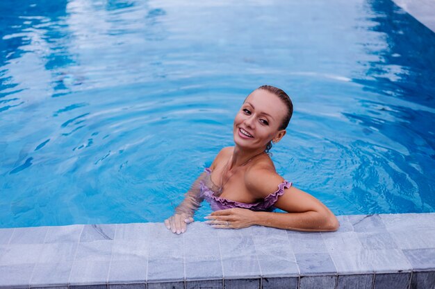 Adatti il ritratto della donna caucasica in bikini nella piscina blu in vacanza alla luce naturale del giorno coudy