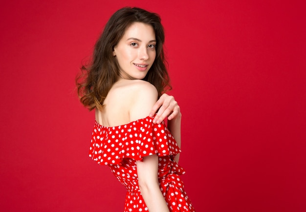 Adatti il ritratto di giovane donna attraente in vestito punteggiato rosso su studio rosso