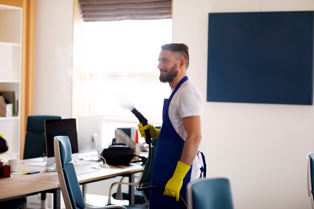 Addetto al servizio di pulizia professionale che utilizza un pulitore a vapore in ufficio