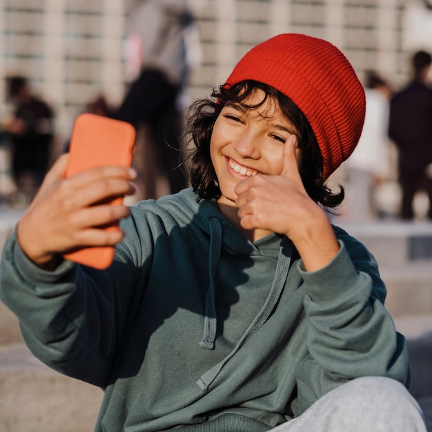 Adolescente all'aperto prendendo selfie dando pollice in alto