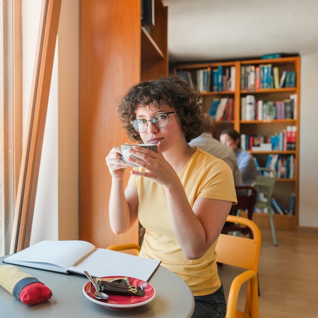 Adolescente con la tazza che studia nella biblioteca