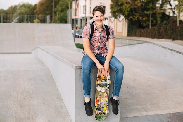 Adolescente con skateboard seduto sul bordo