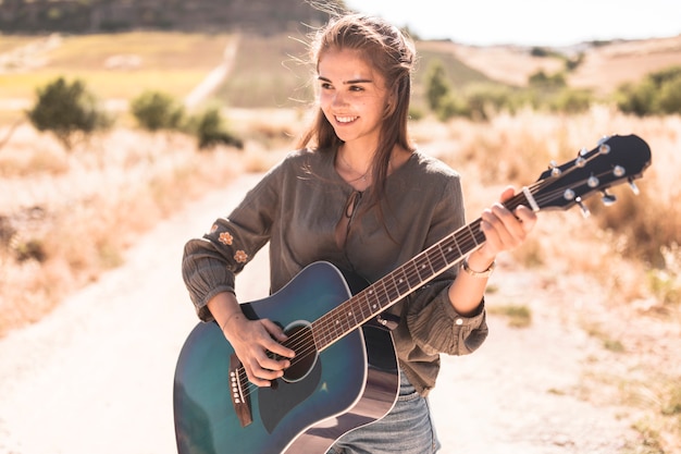 Adolescente felice che gioca chitarra all&#39;aperto