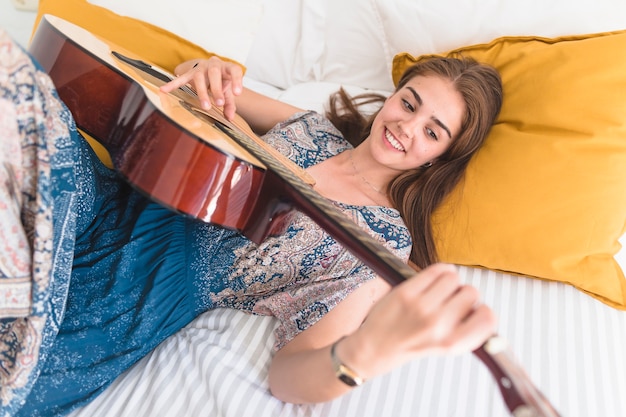 Adolescente felice che si trova sul letto a suonare la chitarra