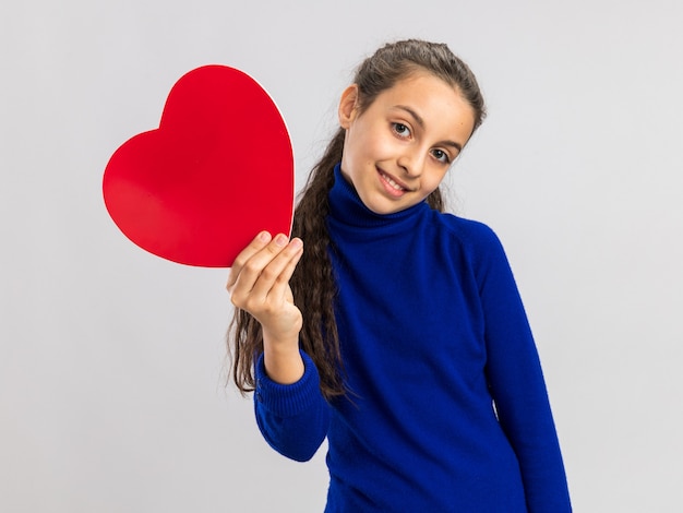 Adolescente felice che tiene a forma di cuore guardando la parte anteriore isolata sul muro bianco