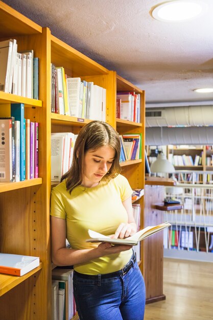 Adolescente femminile che si appoggia su libreria e lettura