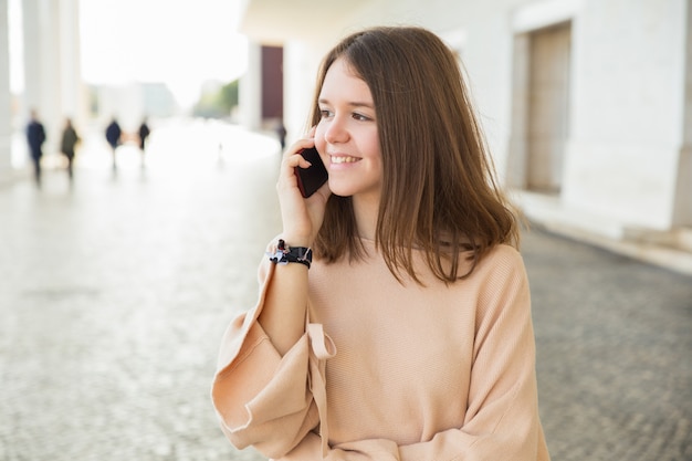 Adolescente femminile sorridente che parla sul telefono cellulare all&#39;aperto