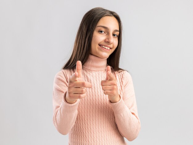 Adolescente graziosa sorridente che guarda la parte anteriore che ti fa gesto isolato sul muro bianco con spazio di copia