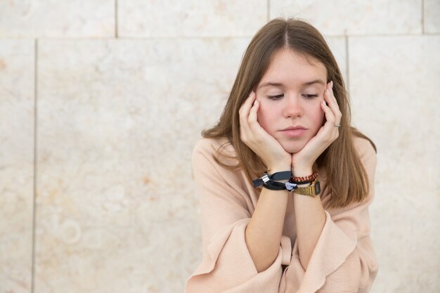 Adolescente pensieroso che si siede alla parete di costruzione all&#39;aperto