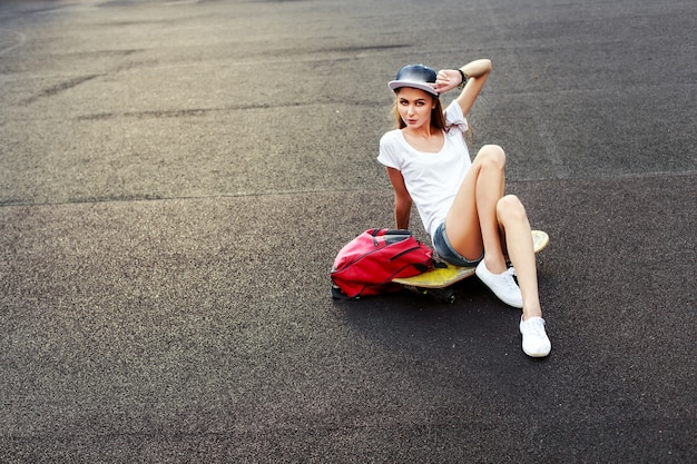 Adolescente seduto su skateboard con una mano che tocca il berretto