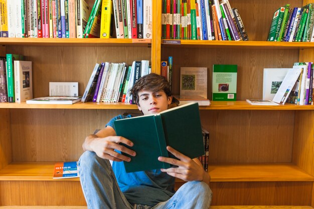 Adolescente sicuro che legge sul pavimento vicino allo scaffale