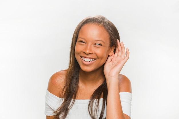 Adolescente sorridente che prova a sentire su fondo bianco