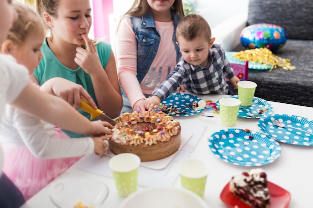 Adolescenti e bambini che assaggiano e tagliano la torta