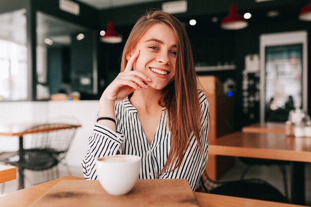 Adorabile affascinante signora con i capelli lunghi che indossa una camicetta alla moda seduto in caffetteria con un grande sorriso