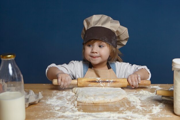 adorabile bambina che stringe le labbra con un aspetto misterioso mentre rotola la pasta da sola