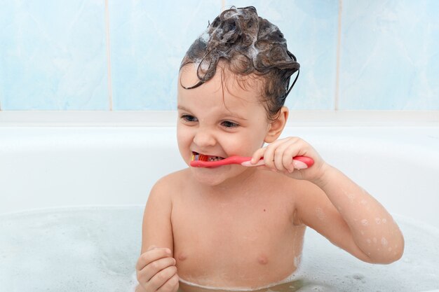 Adorabile bambina lavarsi i denti, fare il bagno, giocando con le bolle di schiuma.