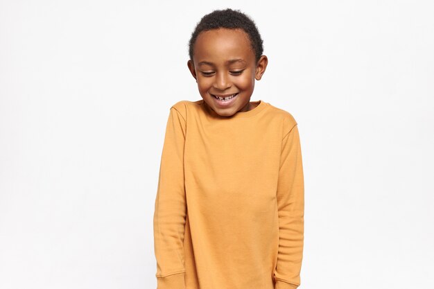 Adorabile bambino afroamericano in maglione giallo che guarda timidamente con timida espressione facciale