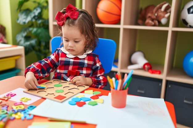 Adorabile bambino biondo che gioca con il gioco di puzzle matematico seduto sul pavimento all'asilo