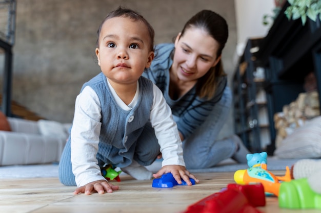 Adorabile bambino che striscia sul pavimento e viene aiutato da sua madre