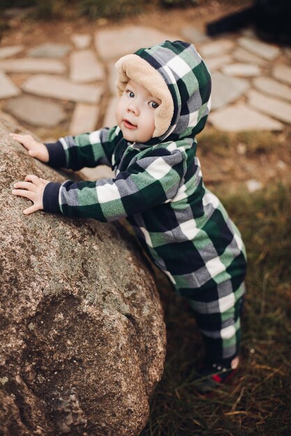 Adorabile bambino in tuta calda con cappuccio seduto sul fogliame