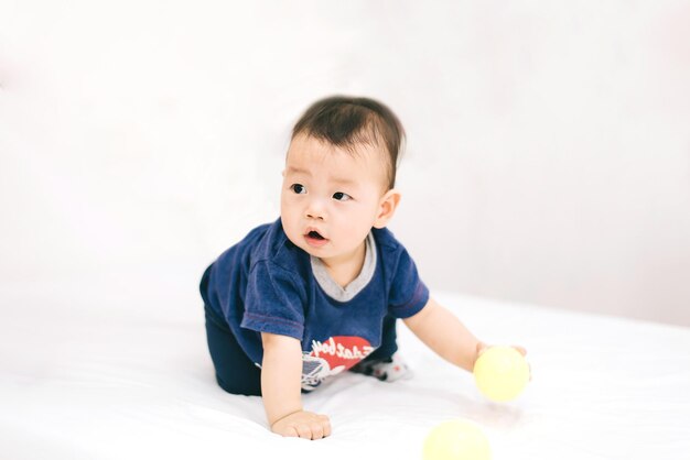 Adorabile bambino paffuto asiatico che gioca una palla di plastica nel soggiorno bianco Si sente divertente e guarda a sua madre e suo padre Tempo felice in famiglia sul concetto di vacanza