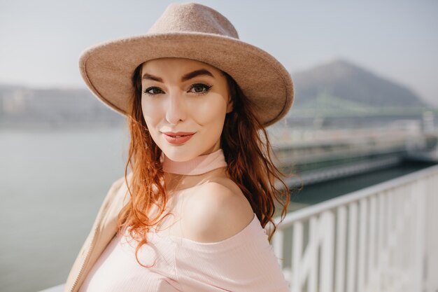 Adorabile donna allo zenzero con trucco alla moda in piedi sulla parete del cielo