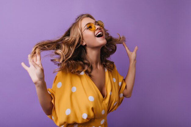 Adorabile donna europea scherzare sulla viola. Ragazza abbronzata alla moda che gioca con i suoi capelli ondulati biondi.