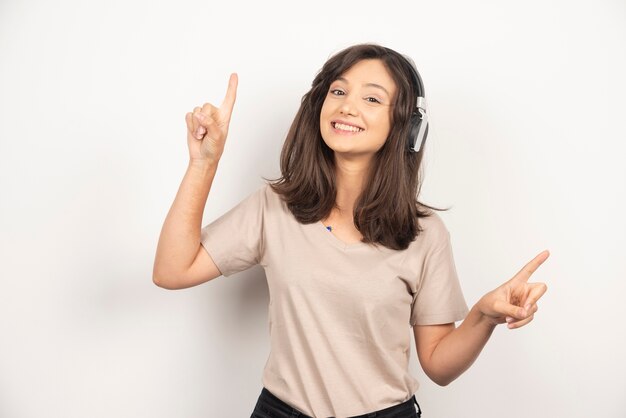 Adorabile donna in camicia beige divertendosi mentre si ascolta la musica utilizzando gli auricolari wireless su sfondo bianco.