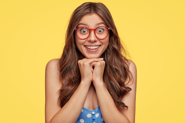 Adorabile giovane donna con gli occhiali in posa contro il muro giallo