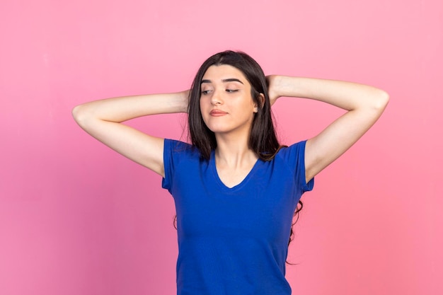 Adorabile ragazza in piedi su sfondo rosa e tenendo le mani dietro la testa Foto di alta qualità