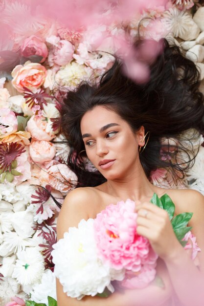 Adorabile ragazza sdraiata su fiori colorati e con in mano un mazzo di fiori Foto di alta qualità