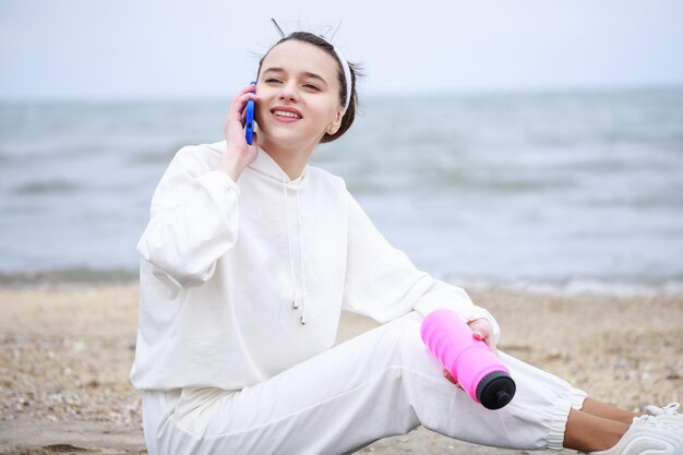 Adorabile ragazza seduta in spiaggia e parlando al telefono Foto di alta qualità