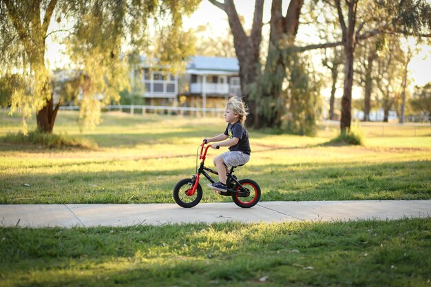 Adorabile ragazzo australiano biondo in sella a una piccola bicicletta nel parco