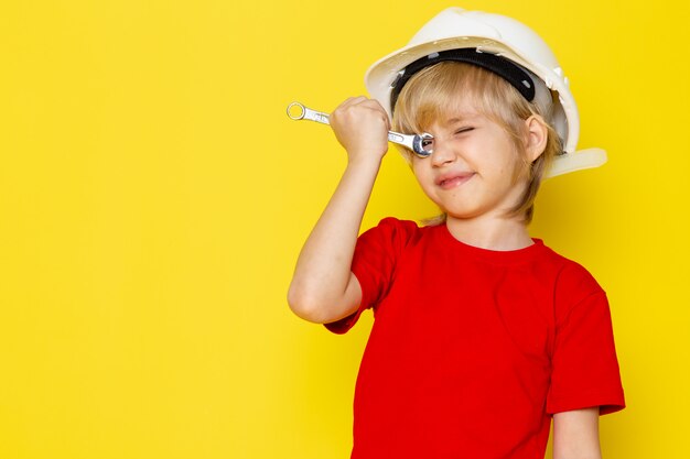 adorabile ragazzo biondo carino in maglietta rossa e casco bianco sul muro giallo