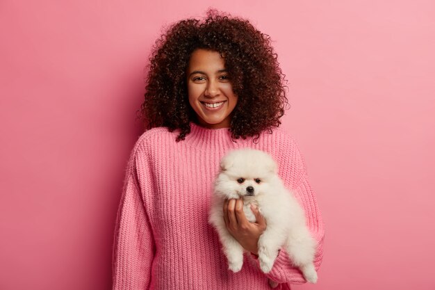 adorabile signora dalla pelle scura in maglione lavorato a maglia, essendo un compagno amichevole per il cane, indossa un maglione rosa