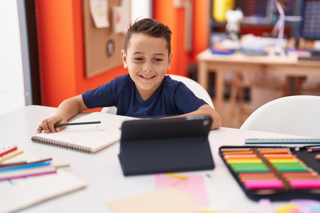 Adorabile studente bambino ispanico che utilizza il touchpad seduto sul tavolo in classe